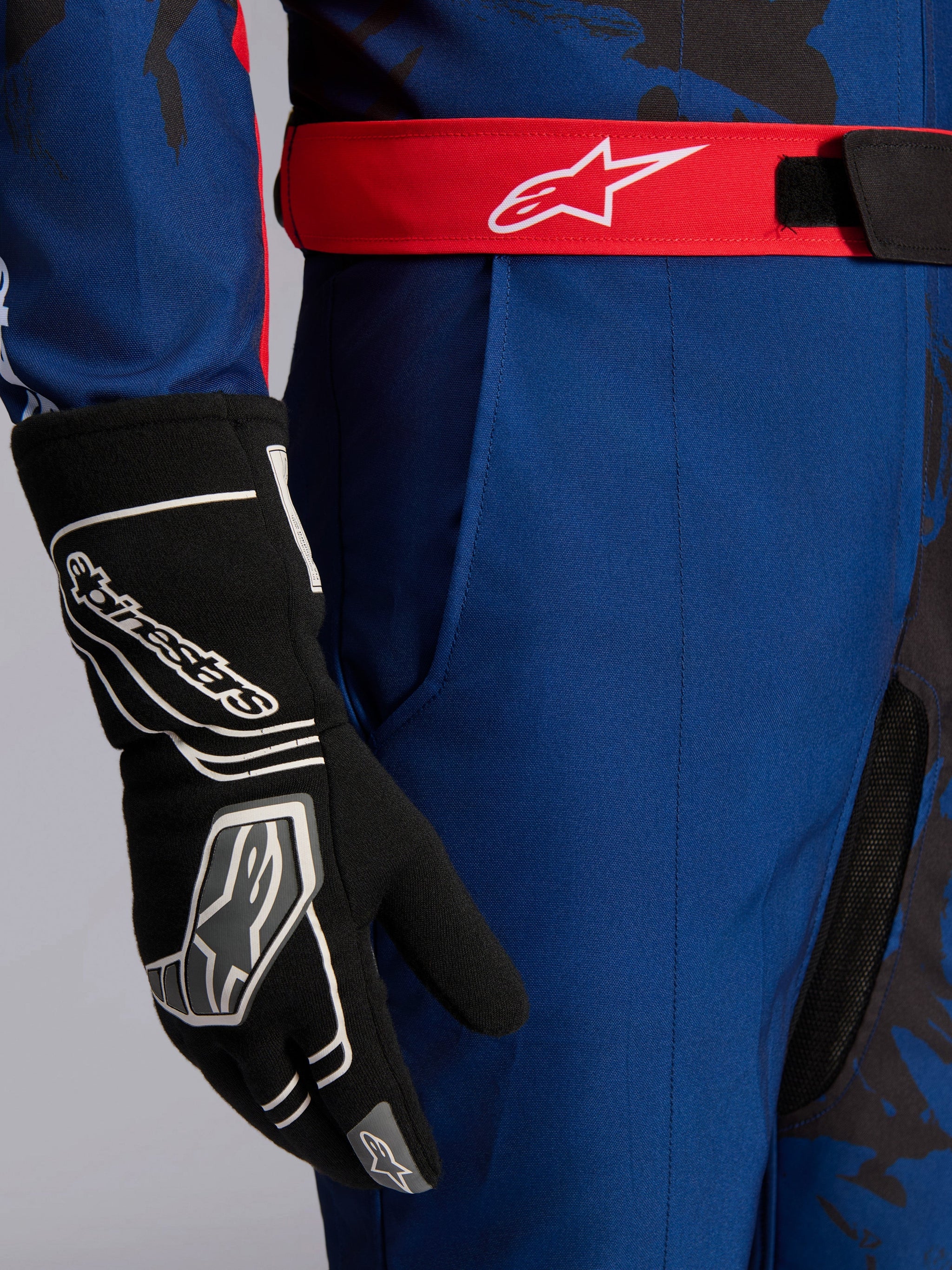 Alpinestars KMX-9 V3 Graphic 5 Suit, Karting Suit, Navy and Red, close-up showing red adjustable waist belt with white logo, worn with black karting glove, featuring durable navy fabric and integrated thigh pocket