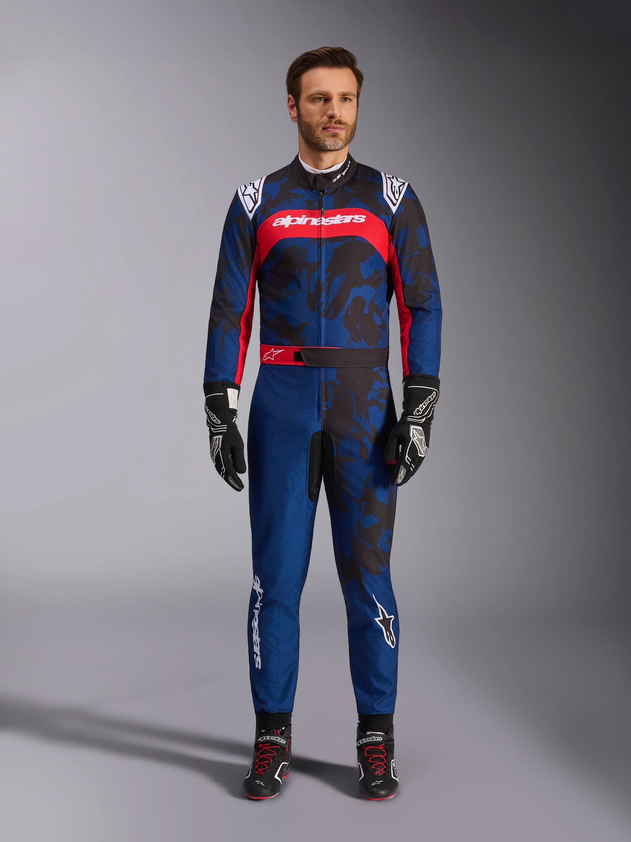 Alpinestars KMX-9 V3 Graphic 5 Suit, Karting Suit in Navy and Red, featuring an abstract camo-style graphic pattern, worn by a model with black racing gloves and shoes, athletic design with prominent Alpinestars branding on the chest and legs.