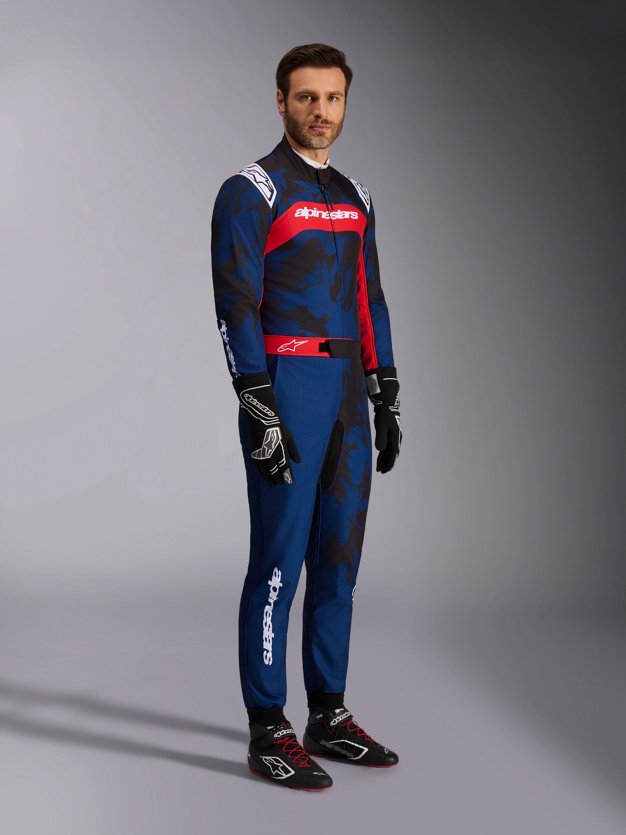 Model wearing the Alpinestars KMX-9 V3 Graphic 5 Suit in Navy Red, full-body shot including black karting gloves and black racing shoes, navy blue suit with dark camo-style graphics and a prominent red chest panel with white branding, professional karting protective gear