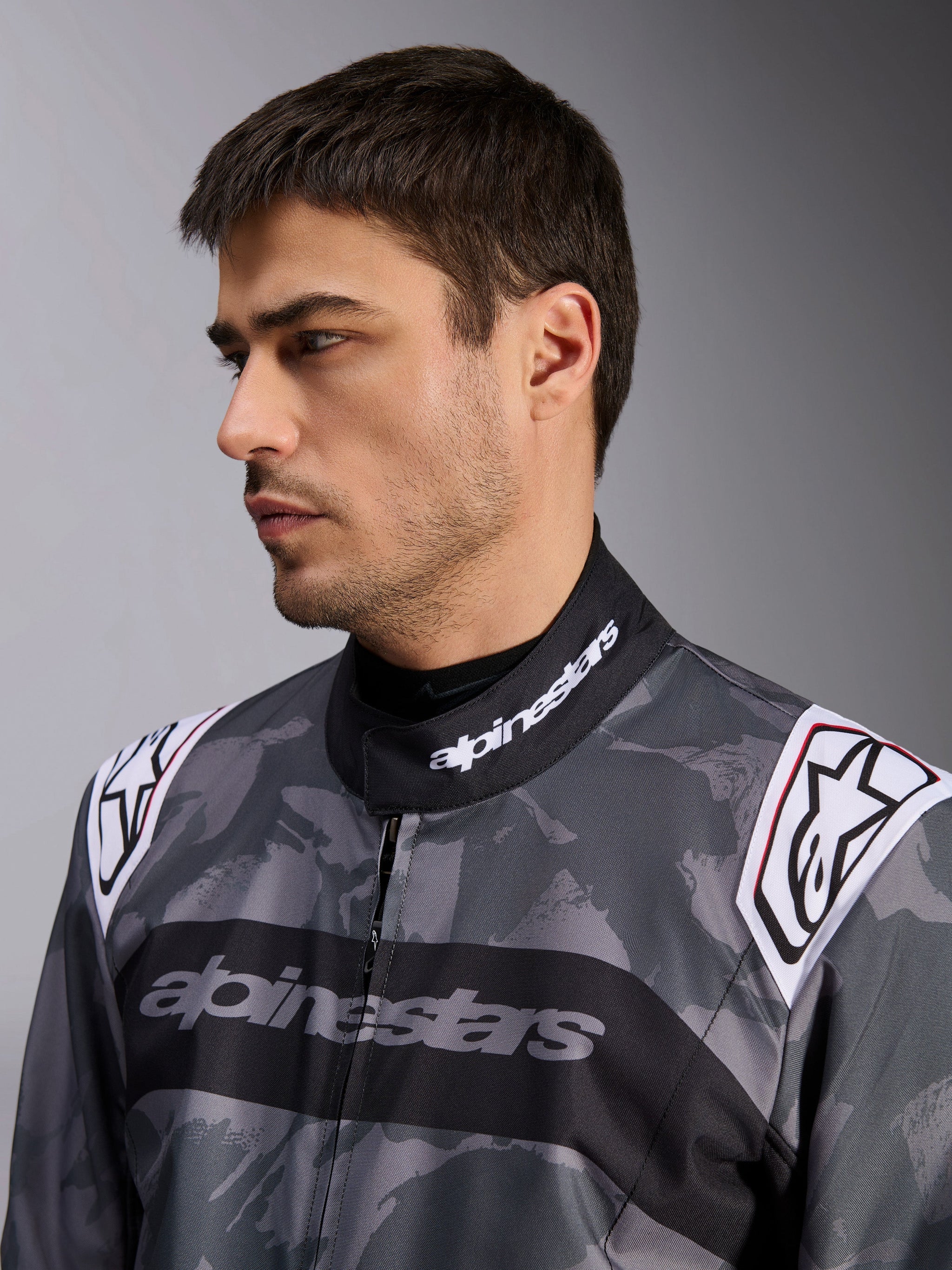 Alpinestars KMX-9 V3 Graphic 5 Suit, Karting Suit, Dark Gray and Black camouflage pattern, close-up of collar and shoulders with white logos, professional racing apparel
