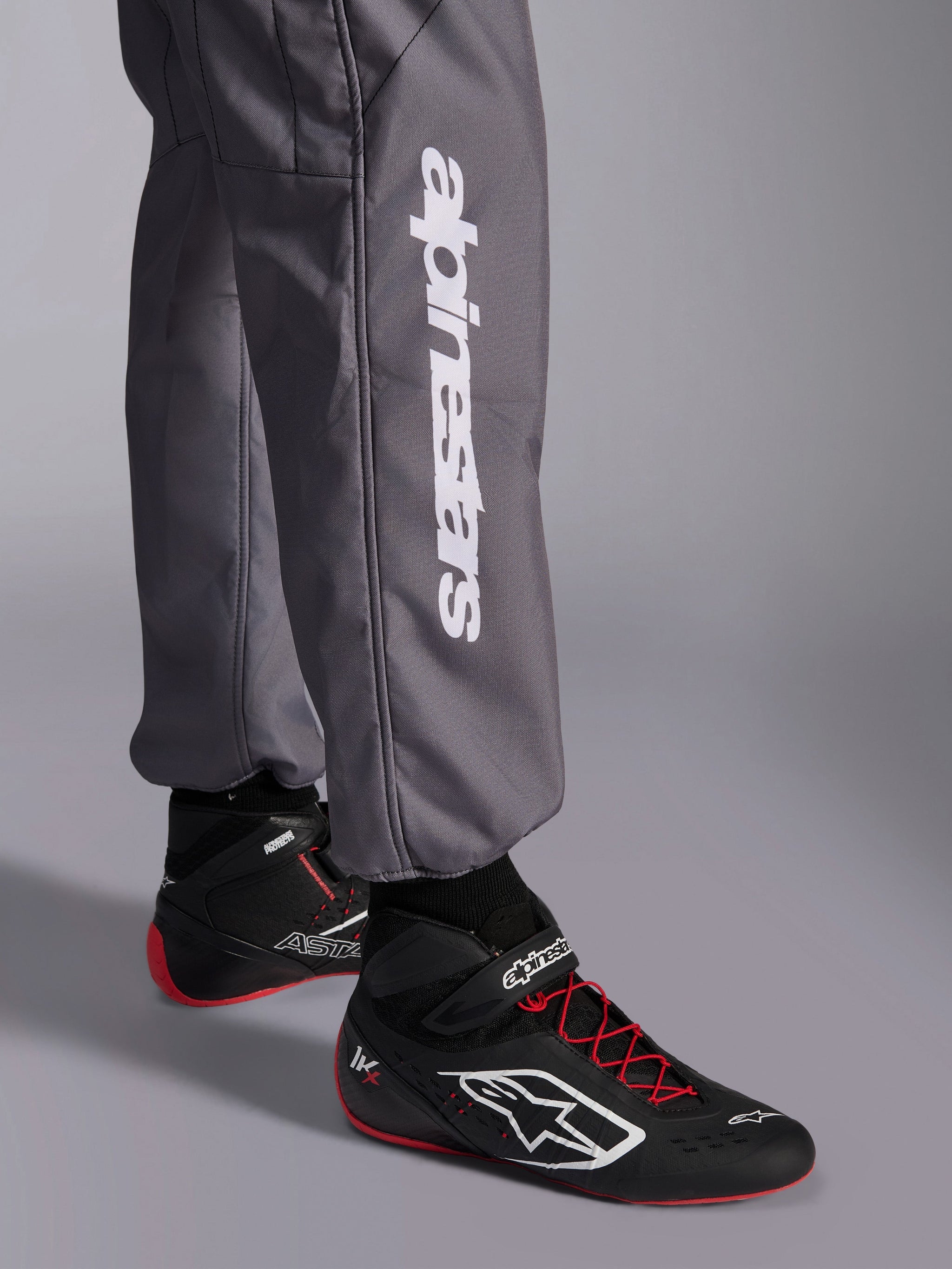 Alpinestars KMX-9 V3 Graphic 5 Suit, Karting Suit, Dark Gray, close-up of lower leg featuring white vertical Alpinestars logo, worn with black and red racing shoes, durable material for karting competition