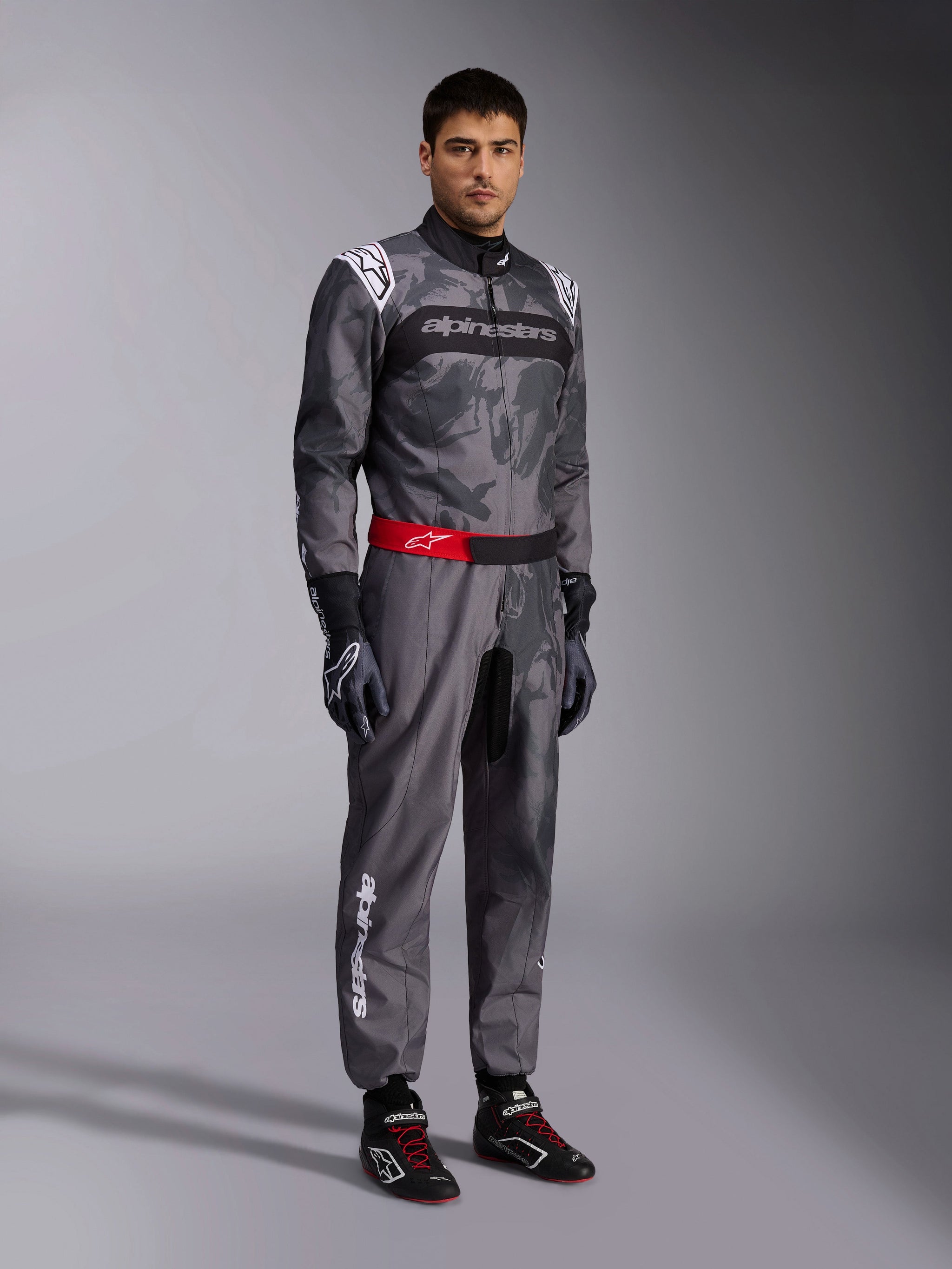 Alpinestars KMX-9 V3 Graphic 5 Suit, Karting Suit, Dark Gray and Black with camo graphic pattern, red waist belt with white logo, worn with racing gloves and shoes, professional motorsport gear for karting