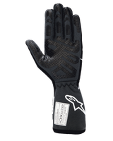 Alpinestars Tech-1 Race V4 Gloves, Professional Auto Racing Gloves, Black Tar Gray, palm side view featuring extensive silicone grip patterns on fingers and palm, extended gauntlet cuff with white Alpinestars logo and FIA/SFI certification labels