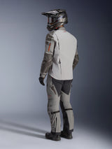 Alpinestars Nazca 3L GORE-TEX PRO Jacket, adventure motorcycle jacket in Dark Gray and Mid Gray, rear three-quarter view on model wearing full riding gear, including matching pants and helmet, technical design with Superfabric reinforcements on elbows.