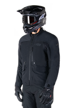 Alpinestars St-7 Prime GORE-TEX Jacket, Black motorcycle jacket, worn by a rider with a black helmet and goggles, featuring large chest cargo pockets and a laminated waterproof shell, premium adventure touring and commuting gear.