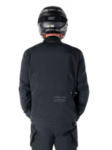 Alpinestars St-7 Prime GORE-TEX Jacket, Black, rear view of a rider, featuring subtle logo and geographic coordinates on the lower back, worn with a matching black helmet and pants, sleek and technical motorcycling apparel