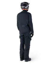 Rear view of a rider wearing the Alpinestars St-7 Prime GORE-TEX Jacket in black, paired with matching black touring pants, a black motorcycle helmet with white logo, and black riding boots, full protective adventure gear for touring and commuting.