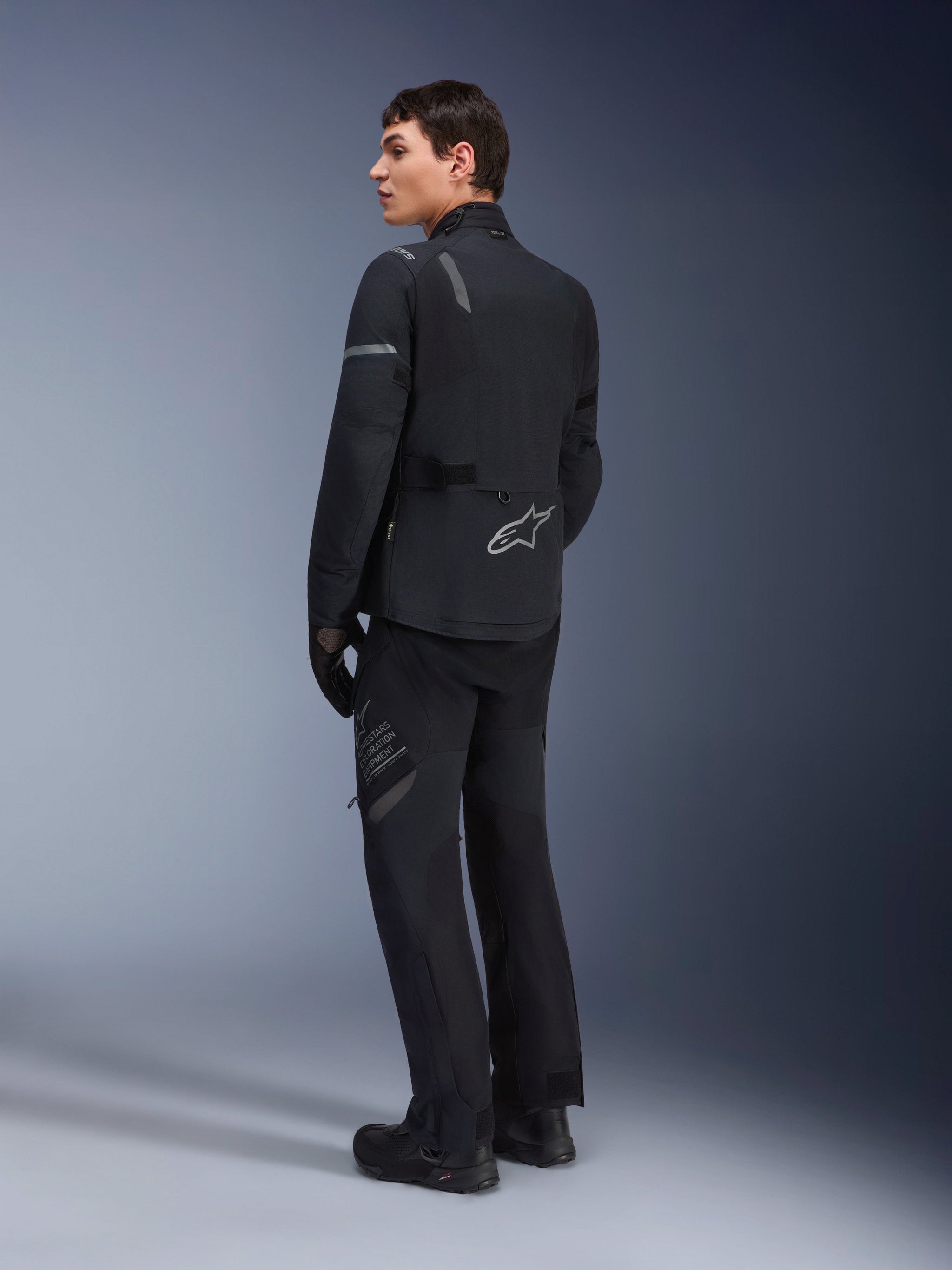 Alpinestars ST-7 2L GORE-TEX Pants, Adventure Touring Pants, Black and Dark Gray, worn with matching ST-7 jacket and black boots, featuring 'Alpinestars Exploration Equipment' branding on the thigh, designed for waterproof and breathable four-season riding.