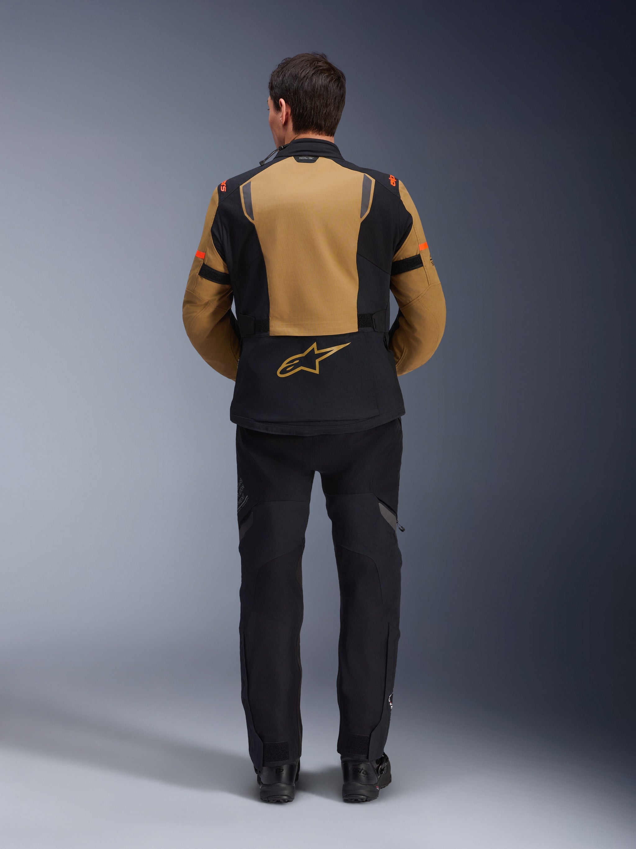 Alpinestars ST-7 2L GORE-TEX Jacket, Adventure Motorcycle Jacket, Gobi Brown and Black, back view showing ergonomic paneling and Alpinestars logo, worn with black riding pants and boots, waterproof touring gear