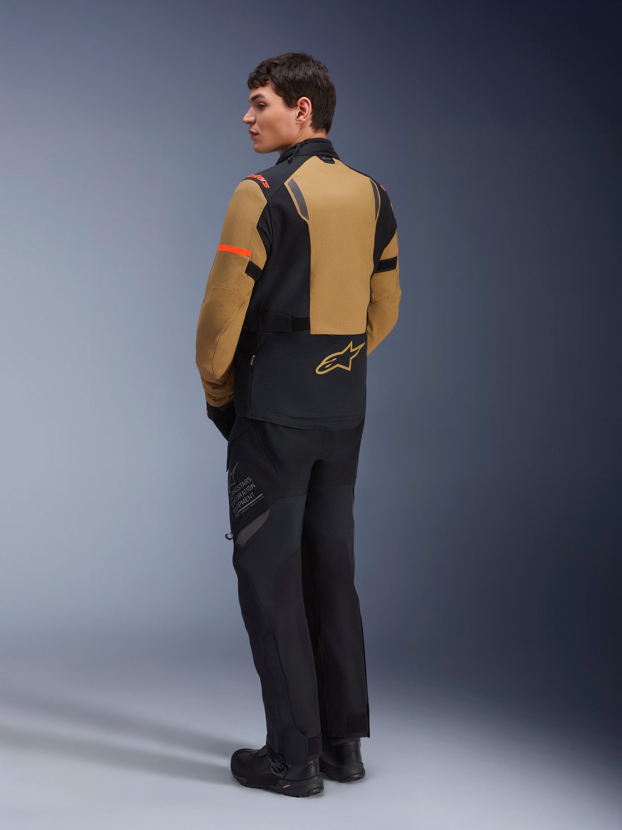 Alpinestars ST-7 2L GORE-TEX Jacket, Adventure Motorcycle Jacket, Gobi Brown and Black, rear view on a model wearing matching riding pants and boots, featuring orange sleeve accents, waterproof laminated shell, and Alpinestars logo, designed for touring and road riding