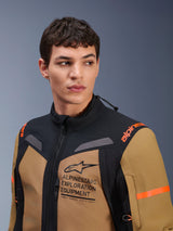 Alpinestars ST-7 2L GORE-TEX Jacket, Gobi Brown and Black, worn by a male model in a studio setting, featuring prominent 'ALPINESTARS EXPLORATION EQUIPMENT' chest branding, orange shoulder logos, and technical waterproof textile construction for adventure riding.
