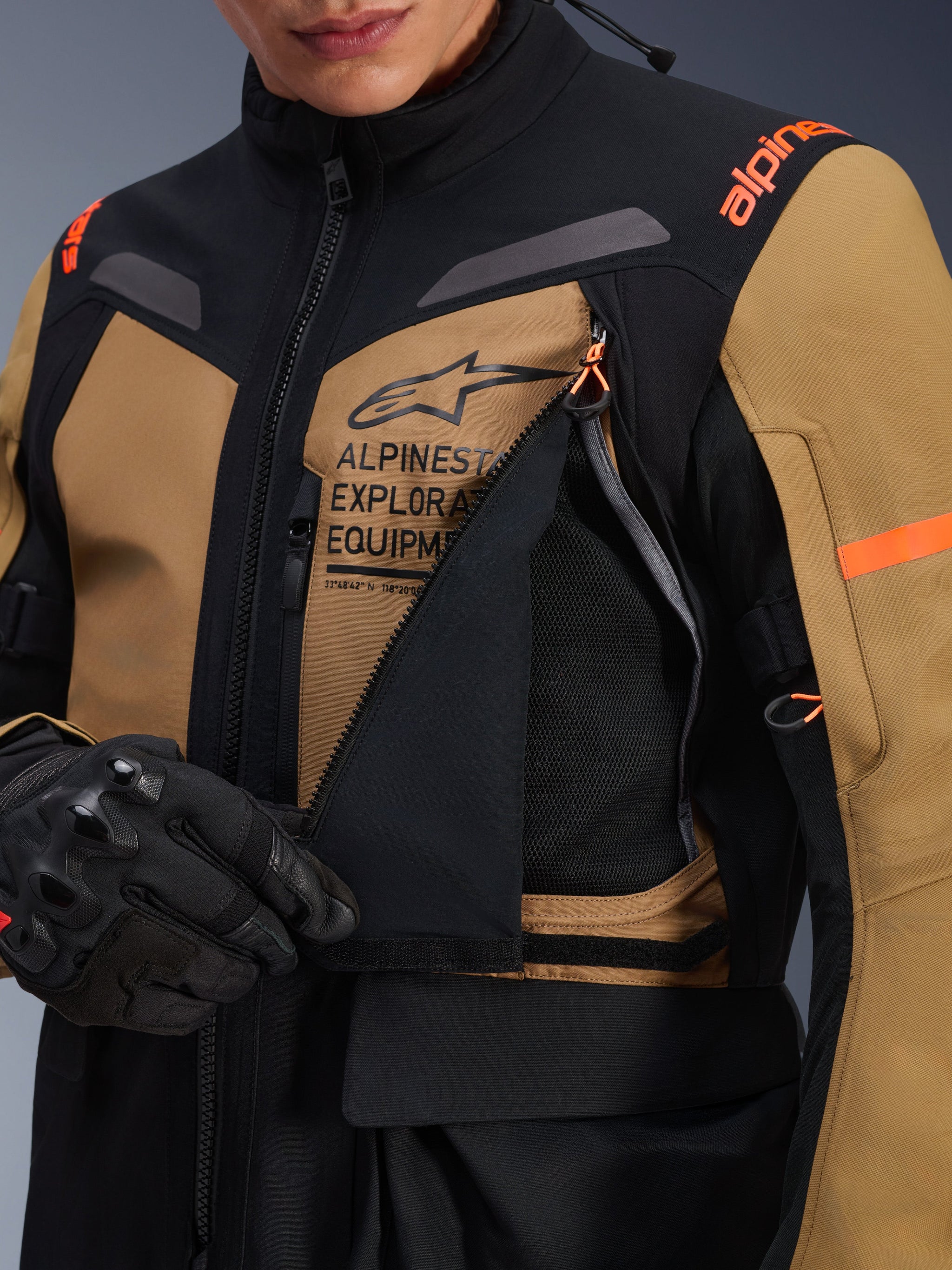 Alpinestars ST-7 2L GORE-TEX Jacket, Adventure Touring Motorcycle Jacket, Gobi Brown and Black, close-up showing the unzipped chest ventilation panel revealing breathable mesh, featuring Alpinestars Exploration Equipment branding and orange accents.