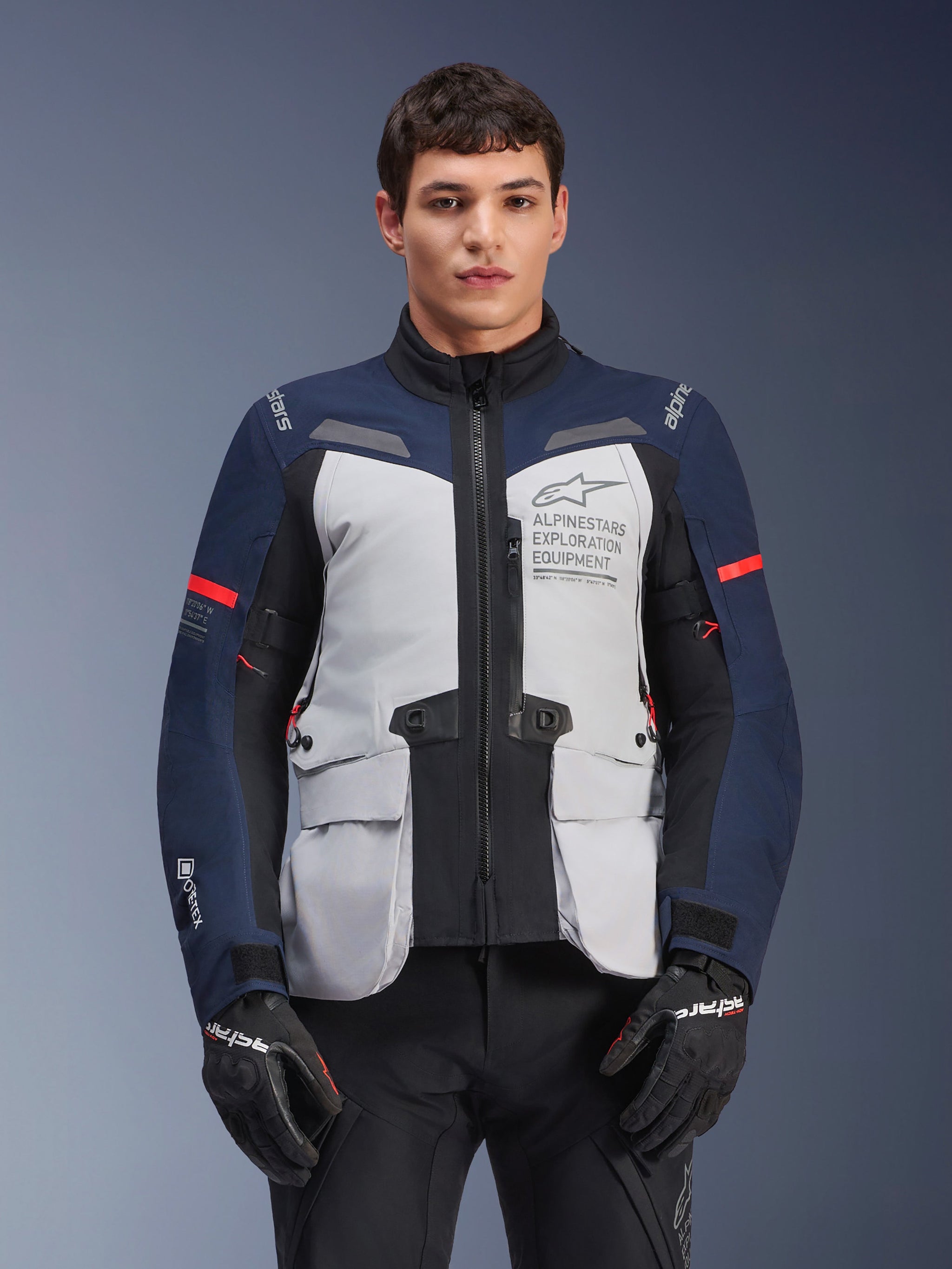 Alpinestars ST-7 2L GORE-TEX Jacket, Motorcycle Adventure Touring Jacket, Ice Gray and Dark Blue with Red accents, Waterproof and breathable, worn by a model with black gloves, featuring Alpinestars Exploration Equipment branding on the chest