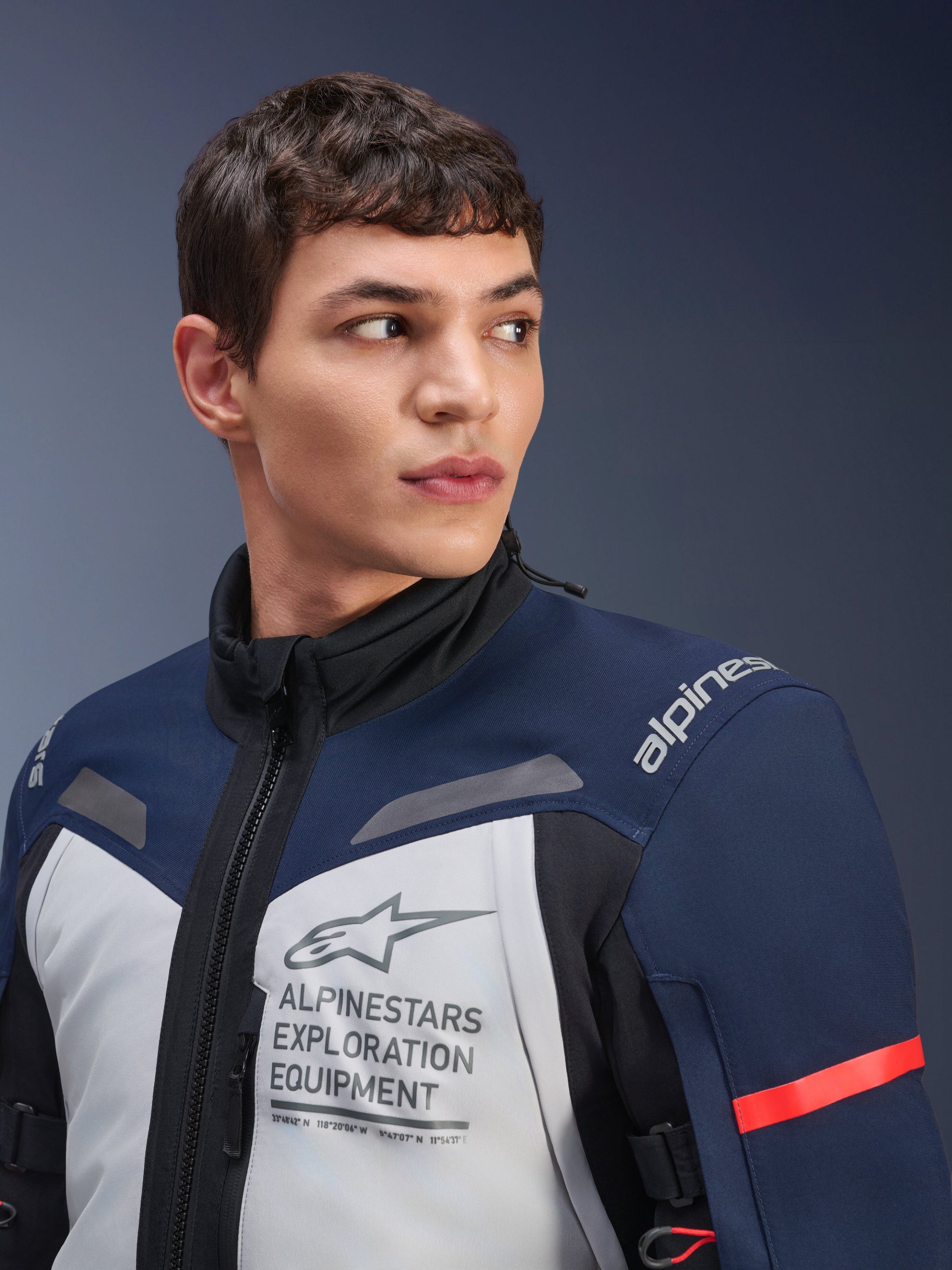 Alpinestars ST-7 2L GORE-TEX Jacket, Ice Gray Dark Blue and Black, worn by male model, featuring Alpinestars Exploration Equipment branding on the chest, high collar, and red accent on sleeve, durable textile design for adventure touring