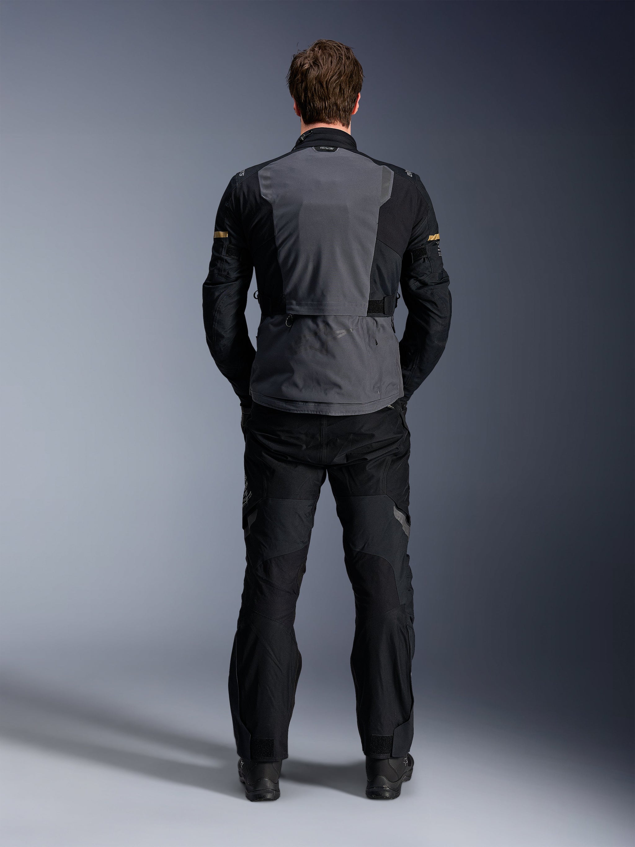 Alpinestars ST-7 2L GORE-TEX Jacket, Deep Gray Black and Dark Khaki, rear view on a model, adventure motorcycle touring jacket with gray back panel and black articulated sleeves, worn with matching black pants.
