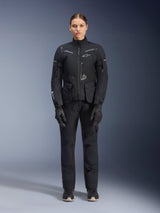 Female rider wearing Alpinestars Women Stella ST-7 2L GORE-TEX Jacket and Pants, Black motorcycle touring outfit, waterproof and breathable technical gear, worn with matching black gloves and boots, full-body protective gear with reflective elements, modern technical design for adventure riding