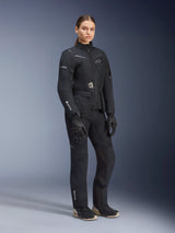 Woman model wearing Alpinestars Stella ST-7 2L GORE-TEX adventure touring suit, Black and Dark Gray jacket and pants, featuring prominent GORE-TEX branding on the sleeve and leg, paired with black gloves and riding boots, professional motorcycle gear designed for all-weather touring.