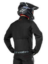 Back view of a rider wearing the Alpinestars Pro-Dura Jacket in Black, durable ripstop textile enduro jacket, featuring a large rear cargo pocket with gray Alpinestars branding across the lower back, paired with a black motocross helmet.