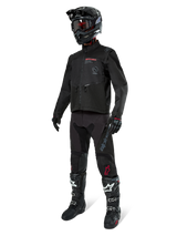 Motocross rider wearing complete racing gear, Alpinestars Pro-Dura Jacket in Black, black pants with grey branding and red accents, black helmet with goggles, and black and white motocross boots, coordinated outfit for enduro and off-road riding