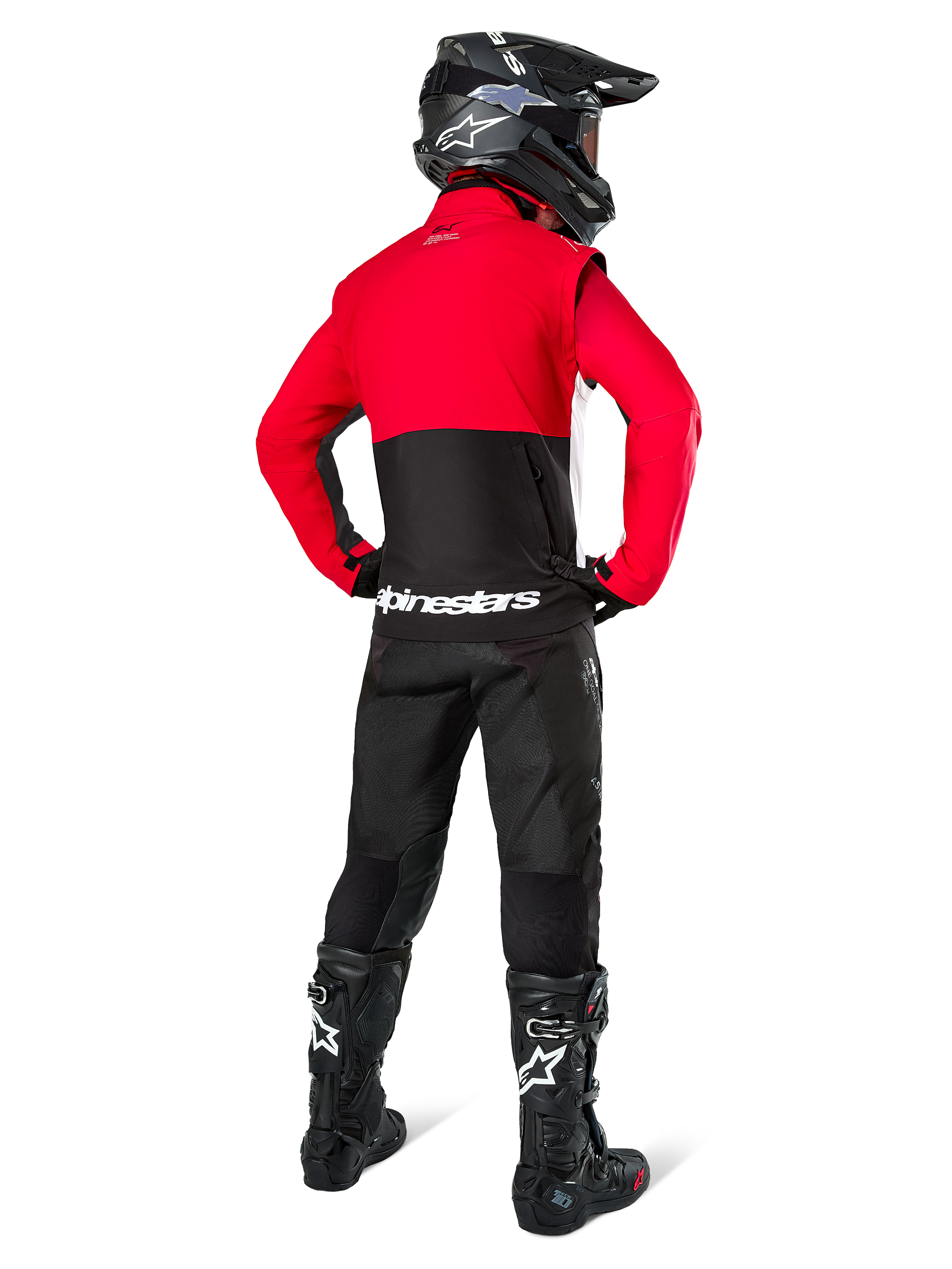 Motocross rider seen from behind wearing the Alpinestars Pro-Dura Jacket in Black, Bright Red, and White, paired with black pants, black helmet, and black off-road boots, featuring a red upper and black lower section with white Alpinestars branding across the back.
