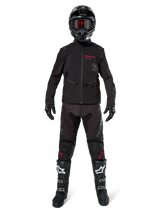 Motocross rider wearing the Alpinestars Lite-Dura Softshell Jacket in Black with red logo details, styled with matching black off-road pants, black helmet, and white and black boots, complete professional enduro racing gear.