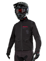 Alpinestars Lite-Dura Softshell Jacket, Black off-road motorcycle jacket with red branding and AS logo, worn with a black motocross helmet, red goggles, and black gloves, featuring zippered hand pockets and adjustable cuffs, designed for enduro riding.