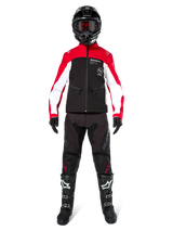 Motocross rider wearing the Alpinestars Lite-Dura Softshell Jacket in Black, Bright Red, and White, coordinated with black off-road pants, black and white boots, and a black helmet with goggles, complete gear setup for enduro racing