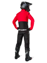 Motocross rider from behind wearing Alpinestars Lite-Dura Softshell Jacket, Black Bright Red and White, featuring a red upper panel and black lower section with white branding, paired with black pants, black helmet, and black boots, coordinated enduro outfit for off-road riding