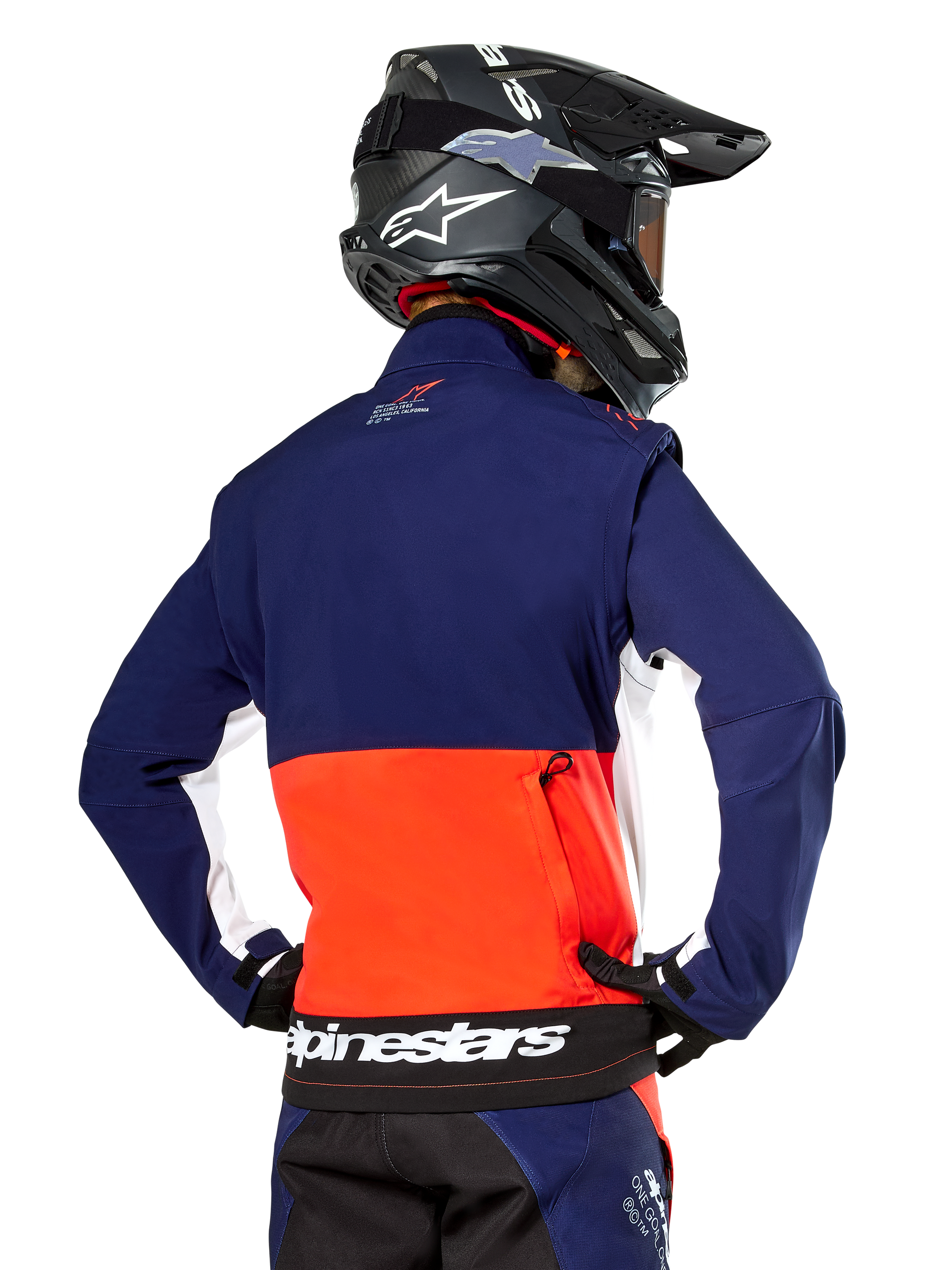 Alpinestars Lite-Dura Softshell Jacket, Navy Hot Orange and White, rear view worn by a motocross rider, featuring a large white logo on the back hem and zippered storage pocket, part of a complete off-road racing outfit.