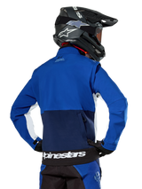 Alpinestars Lite-Dura Softshell Jacket in Navy, Bright Blue, and White, rear view showing the large zippered back pocket for sleeve storage, white side accents, and Alpinestars branding on the hem, worn with a black motocross helmet and matching gear.