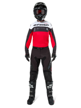 Motocross rider wearing Alpinestars Pro-Dura Pants in Black and Magnet, paired with a red, white, and black jersey, black helmet, and black boots, full off-road racing gear kit, durable and lightweight design for enduro riding