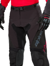 Close-up of Alpinestars Pro-Dura Pants, Enduro Pants, Black Magnet White with red accents, featuring a secure magnetic buckle closure and zip fly, worn with matching red jersey and black gloves, durable ripstop construction for off-road riding