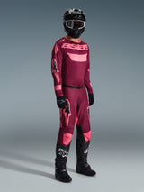 Motocross rider wearing complete racing gear, Alpinestars 2026 Racer Riway Jersey in Dark Red Coral with pink accents, matching dark red pants with pink logos, black helmet with white-rimmed goggles, black gloves, and black boots with white logos, coordinated outfit for off-road racing