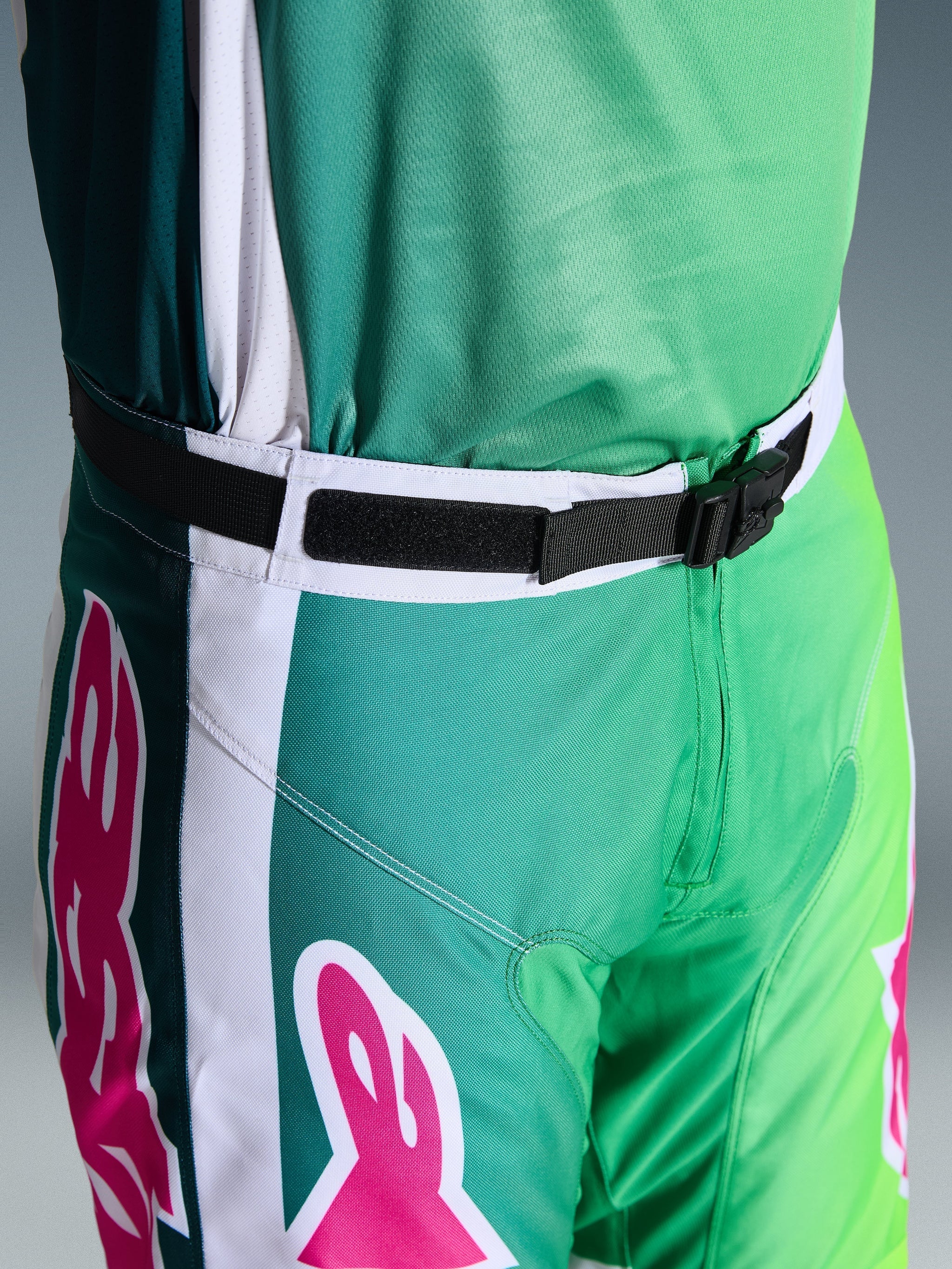 Alpinestars 2026 Racer Portl Pants, Motocross Pants, Green White and Black with Pink logo accents, close-up of the waist showing the SX2 magnetic buckle and adjustable closure, durable gear for off-road racing