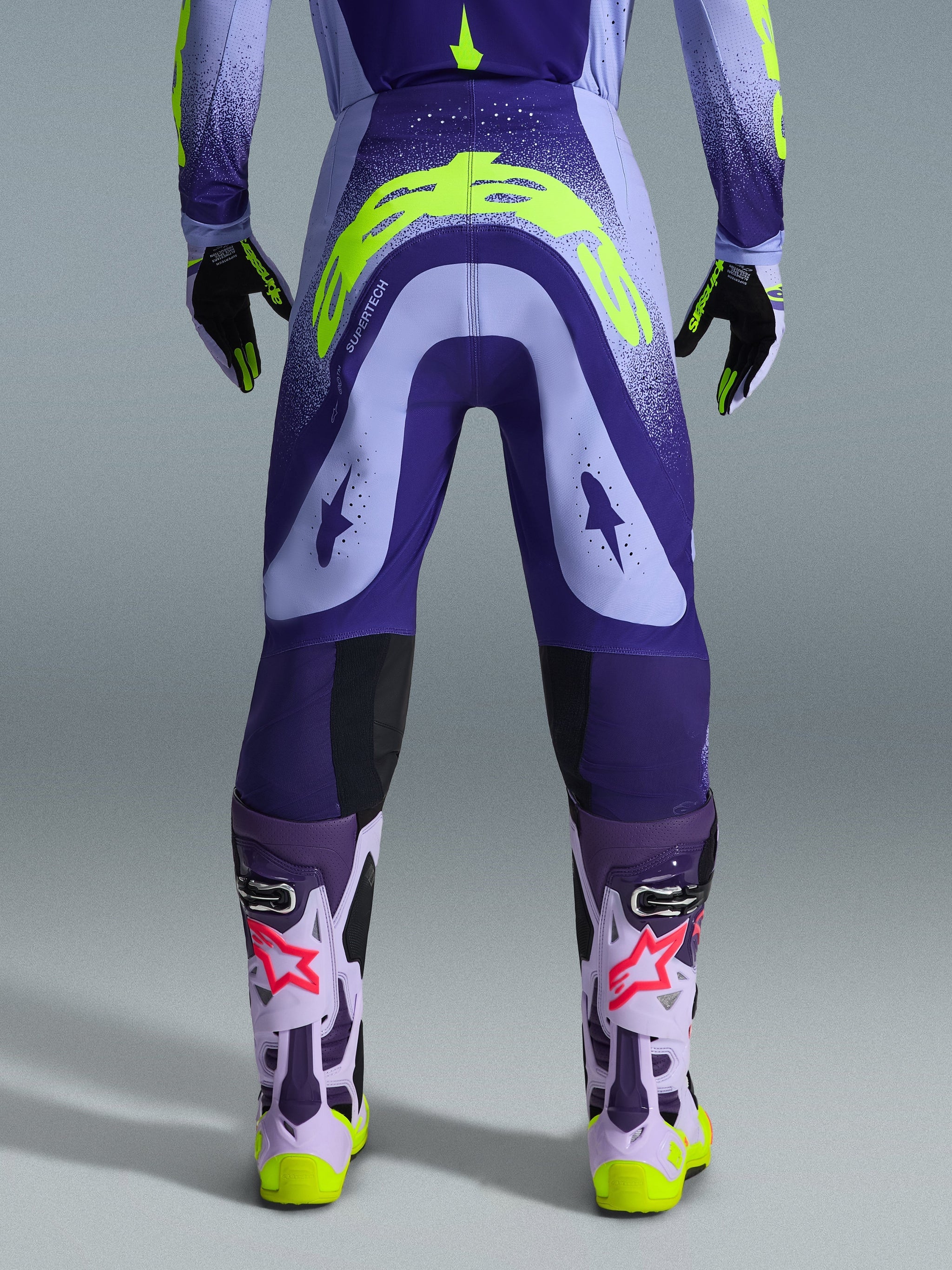 Alpinestars 2026 Supertech Scenz Pants, Motocross Pants, Purple and Yellow Fluo, rear view showing large yellow logo on seat, worn with matching jersey, gloves, and protective boots, athletic fit for professional motocross racing.
