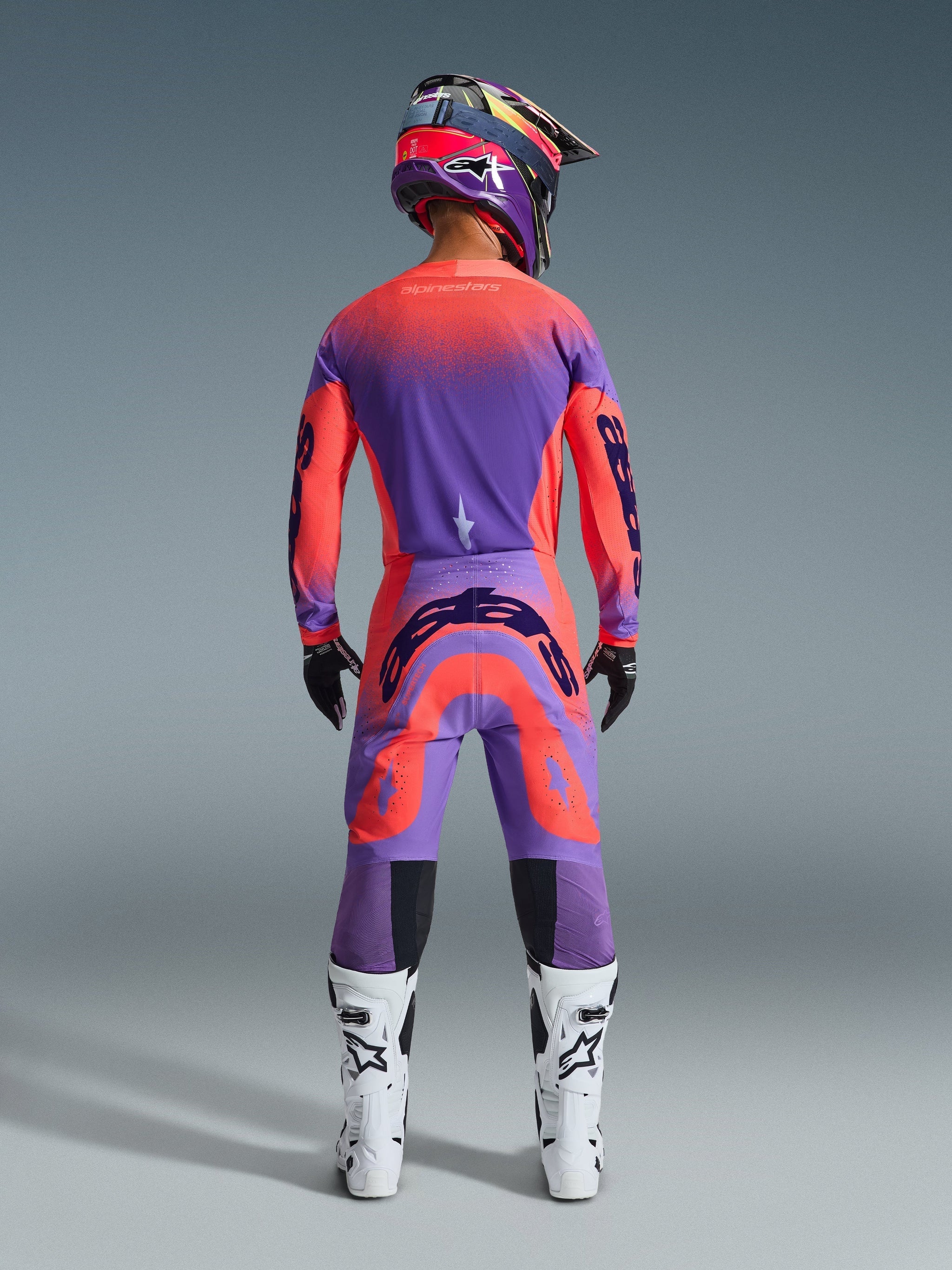 Alpinestars 2026 Supertech Scenz Pants, Motocross Pants, Hot Coral and Purple, rear view of motocross rider wearing a complete racing gear set, featuring vibrant gradient design with bold rear logos, paired with a matching jersey, helmet, and white boots.