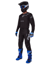 Motocross rider wearing complete Alpinestars racing gear, 2025 Racer Graphite Pants in Black and Gray, matching black jersey with grey logos, black helmet with blue goggles, bright blue and purple boots, and blue and grey gloves, coordinated outfit for off-road racing