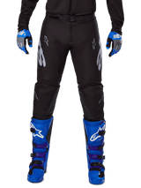 Alpinestars 2025 Racer Graphite Pants, Motocross Pants, Black and Gray, worn with blue and gray gloves and blue boots, featuring silver Astars branding on the thighs and reinforced knees, sporty design for off-road performance