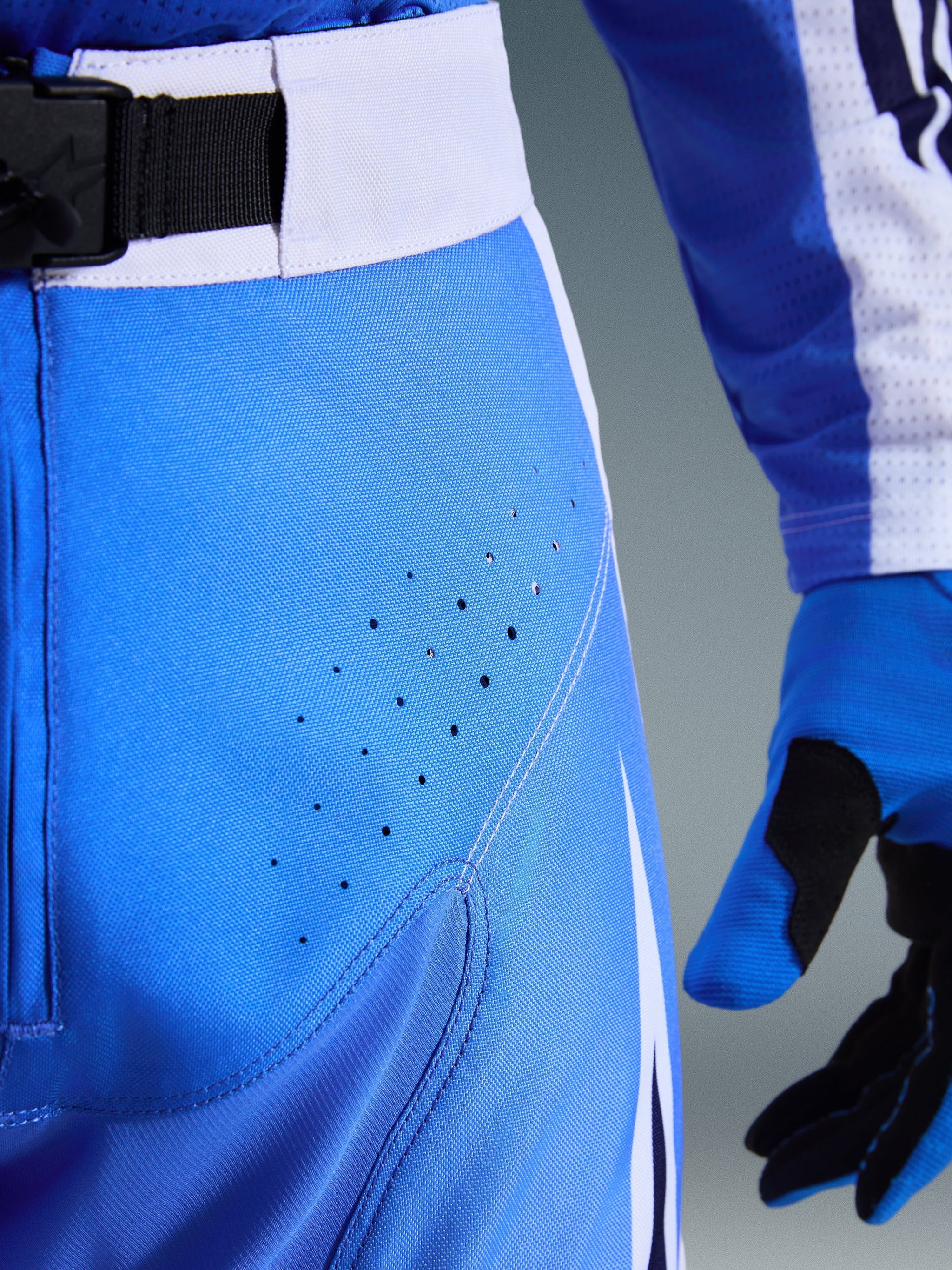 Alpinestars 2026 Techstar Knif Pants, Ucla Blue and White, close-up of hip area showing laser-cut perforations for ventilation, SX2 magnetic buckle waist closure, and matching motocross gloves