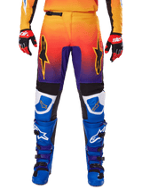 Alpinestars 2025 Fluid Wurx Pants, Motocross Pants, Multicolor featuring orange-to-purple gradient and blue panels, worn with matching blue and purple boots and red and black gloves, front view with star logo branding.