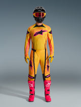 Motocross rider wearing full Alpinestars 2026 Techstar Nomur gear set, Orange Yellow and Pink jersey and pants, matching yellow and pink gloves, vibrant pink racing boots, and black helmet with pink goggles, coordinated high-performance motocross outfit.