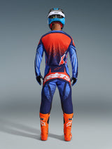 Motocross rider seen from the back wearing Alpinestars 2026 Techstar Nomur Pants in Dark Navy, Orange, and UCLA Blue, styled with a matching jersey and bright orange boots, professional off-road racing gear set.