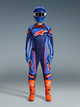 Alpinestars 2026 Techstar Nomur gear set, Motocross rider in full racing kit, Dark Navy with Orange and UCLA Blue accents, matching jersey and pants with large logos, blue helmet and bright orange boots, coordinated off-road competition gear.