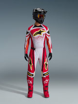 Motocross rider wearing Alpinestars 2026 Techstar Nomur Pants, Red White and Black off-road racing gear, matching jersey with yellow star logo, black helmet with goggles, red boots, and black gloves, coordinated outfit for motocross