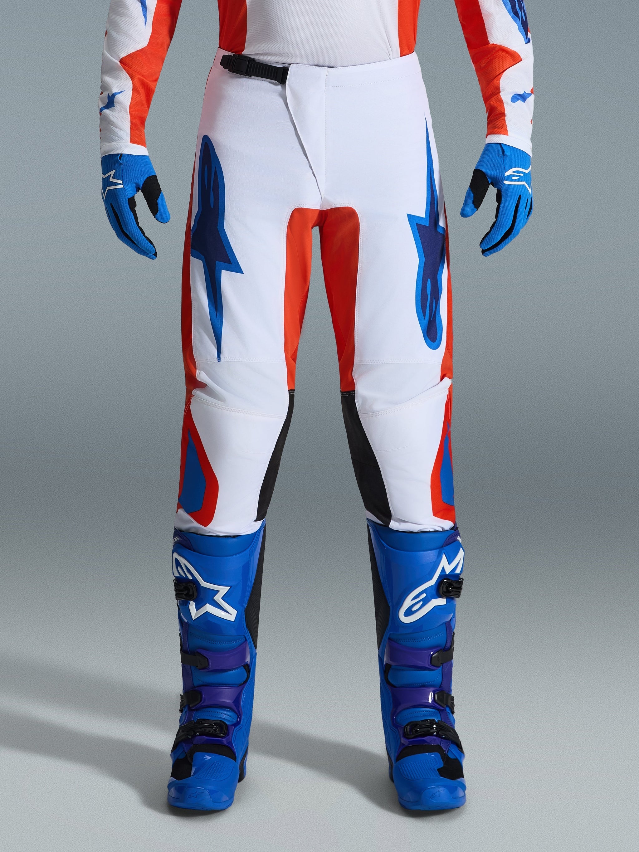 Alpinestars 2026 Fluid Grid Pants, Motocross Pants, Orange and UCLA Blue, worn with matching blue boots and gloves, featuring white chassis with bold blue logos and orange accents, ergonomic design for off-road performance