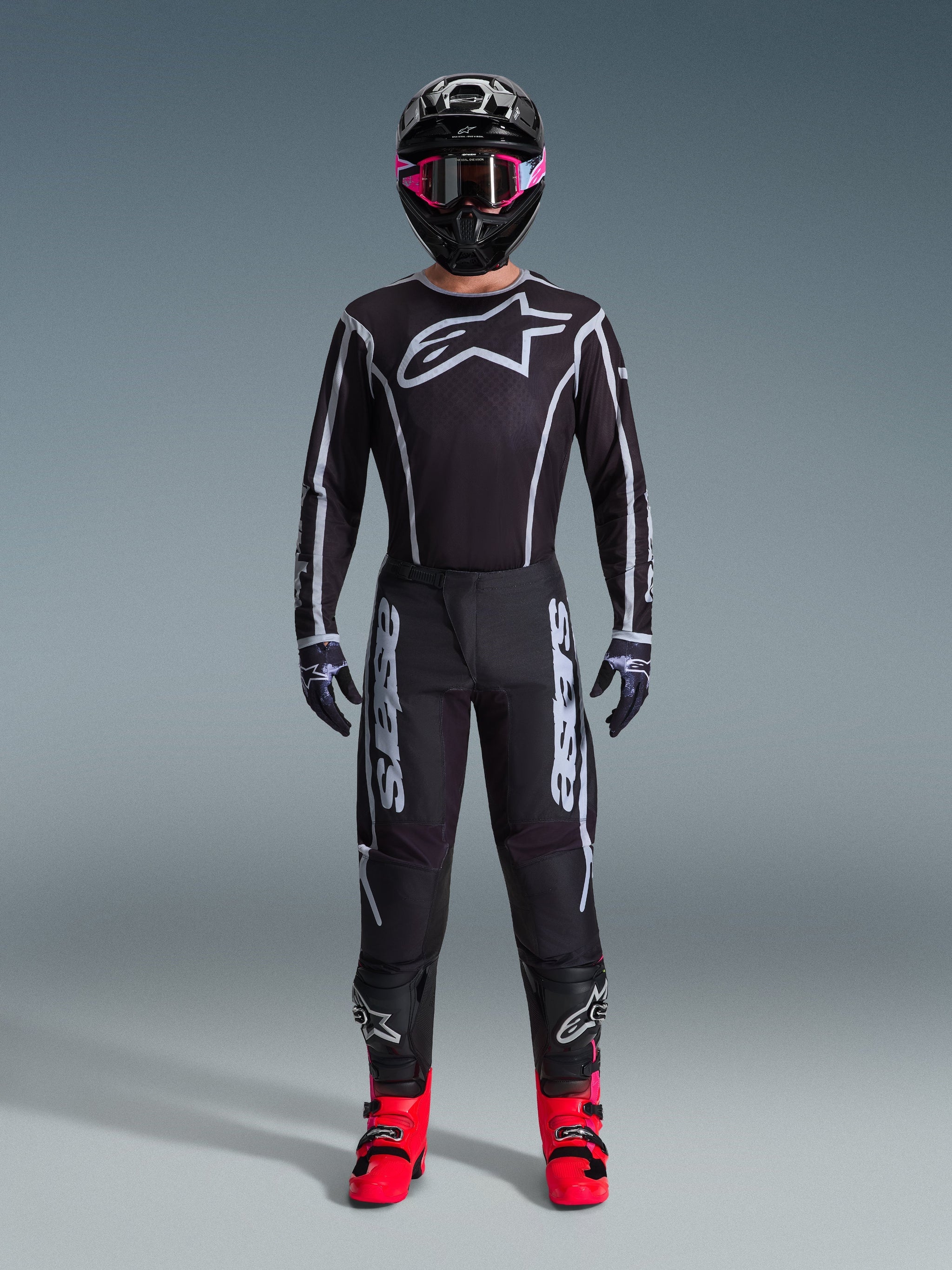 Alpinestars 2026 Fluid Apex Gear Set, Motocross Outfit, Black with Gray accents, jersey featuring large white Astars logo, matching pants with bold branding, black helmet with pink goggles, and bright red boots, complete off-road racing kit