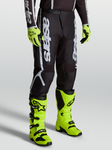 Alpinestars Fluid Apex V2 Pants, Men’s Motocross Gear in Black and Silver, featuring Alpinestars branding and durable 600D polyfabric. Shown on-model with bright yellow boots.