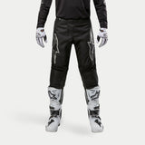 Alpinestars 2024 Fluid Graphite Pants, Motocross Pants, Black and Silver, featuring silver Alpinestars logos on the thighs, worn with white and black motocross boots and gloves, sporty design for off-road racing