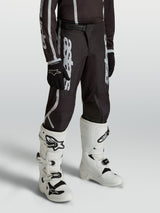 Alpinestars Youth Fluid Apex V2 Pants, black and silver motocross gear for young riders, featuring an ergonomic pre-curved fit.