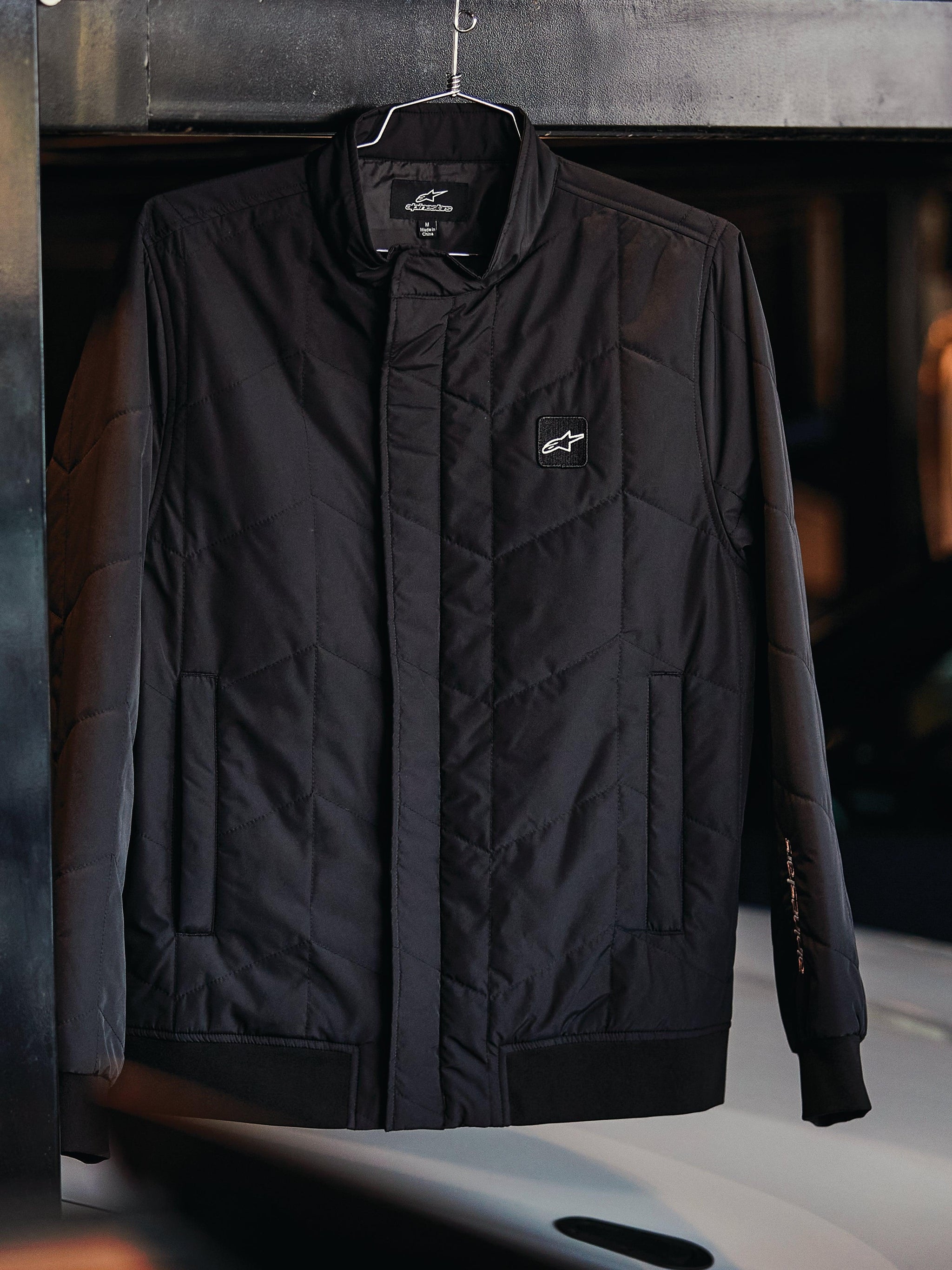 Alpinestars Precedent Jacket, Quilted Sportswear Jacket, Black, featuring an angled quilt pattern, low track collar with covered zipper, chest logo patch, and ribbed cuffs and hem, motorsport-inspired design